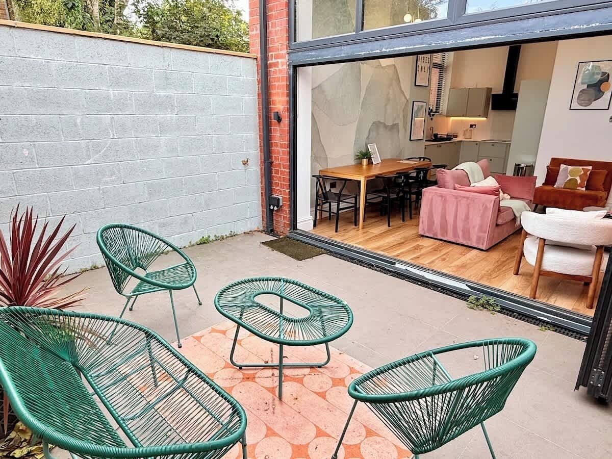 A patio with green chairs, a wooden table, and a pink sofa inside a house.