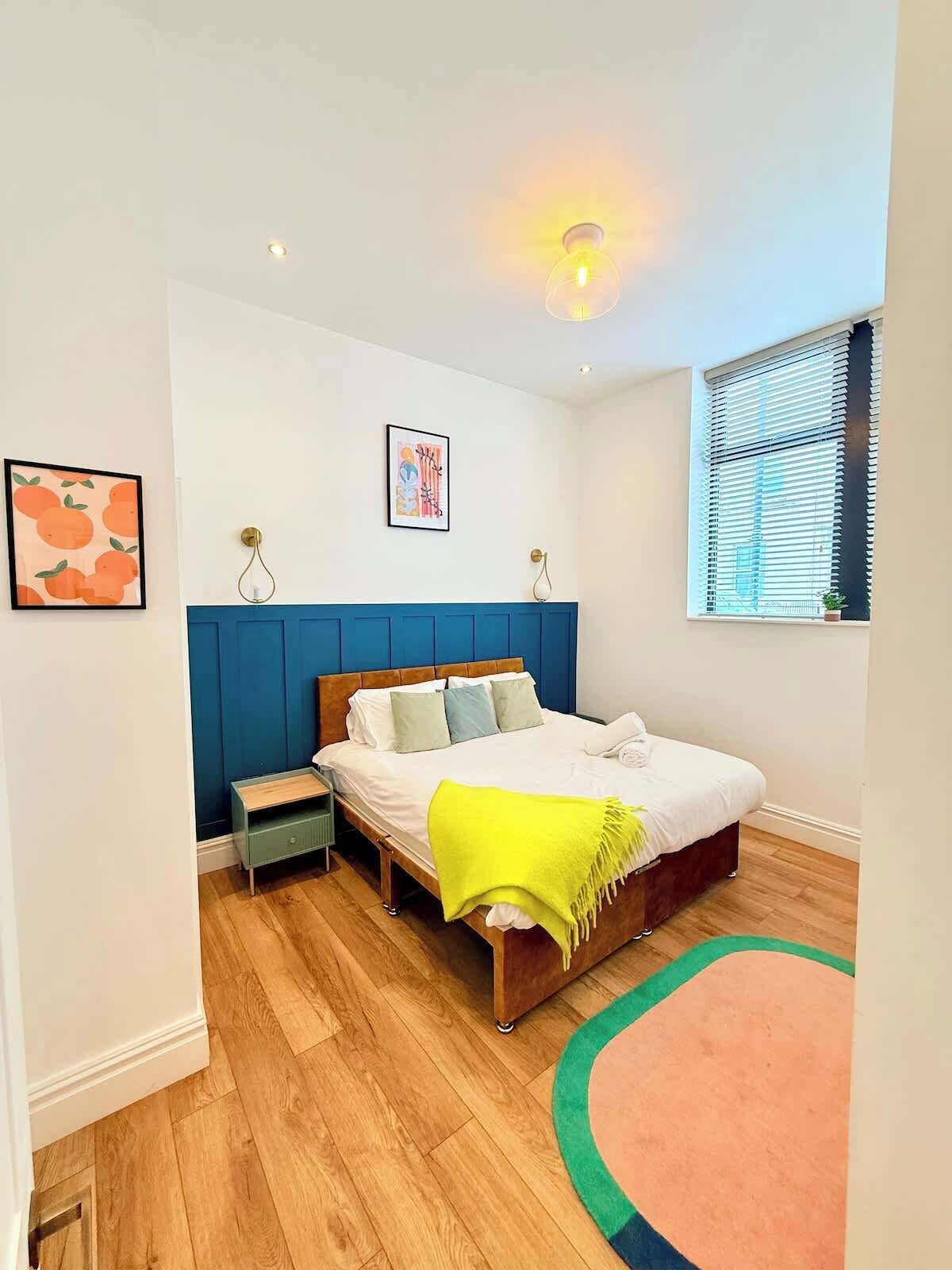 Ein Schlafzimmer mit Bett, Nachttischen, Fenster mit Jalousien und einer Wandleuchte.