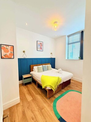 Ein Schlafzimmer mit Bett, Nachttischen, Fenster mit Jalousien und einer Wandleuchte.