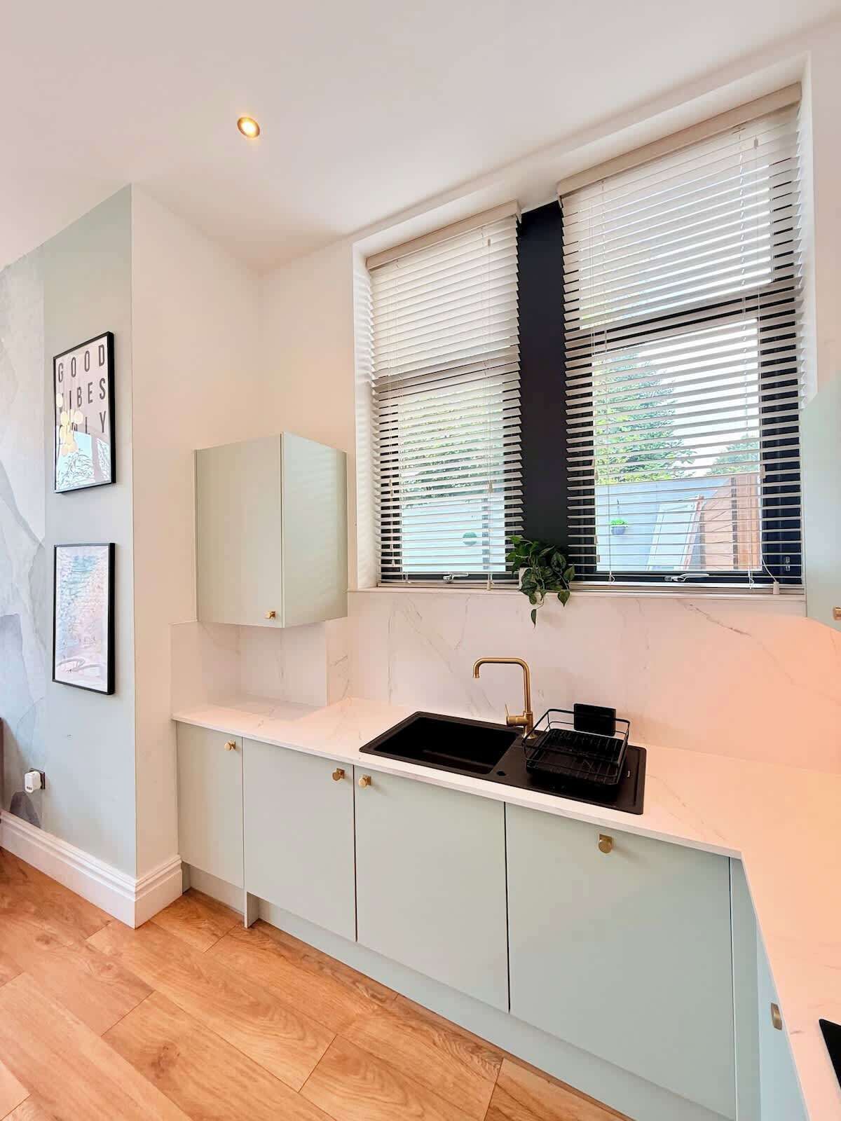 Una cocina moderna con pileta integrada, muebles blancos y ventana con persianas.