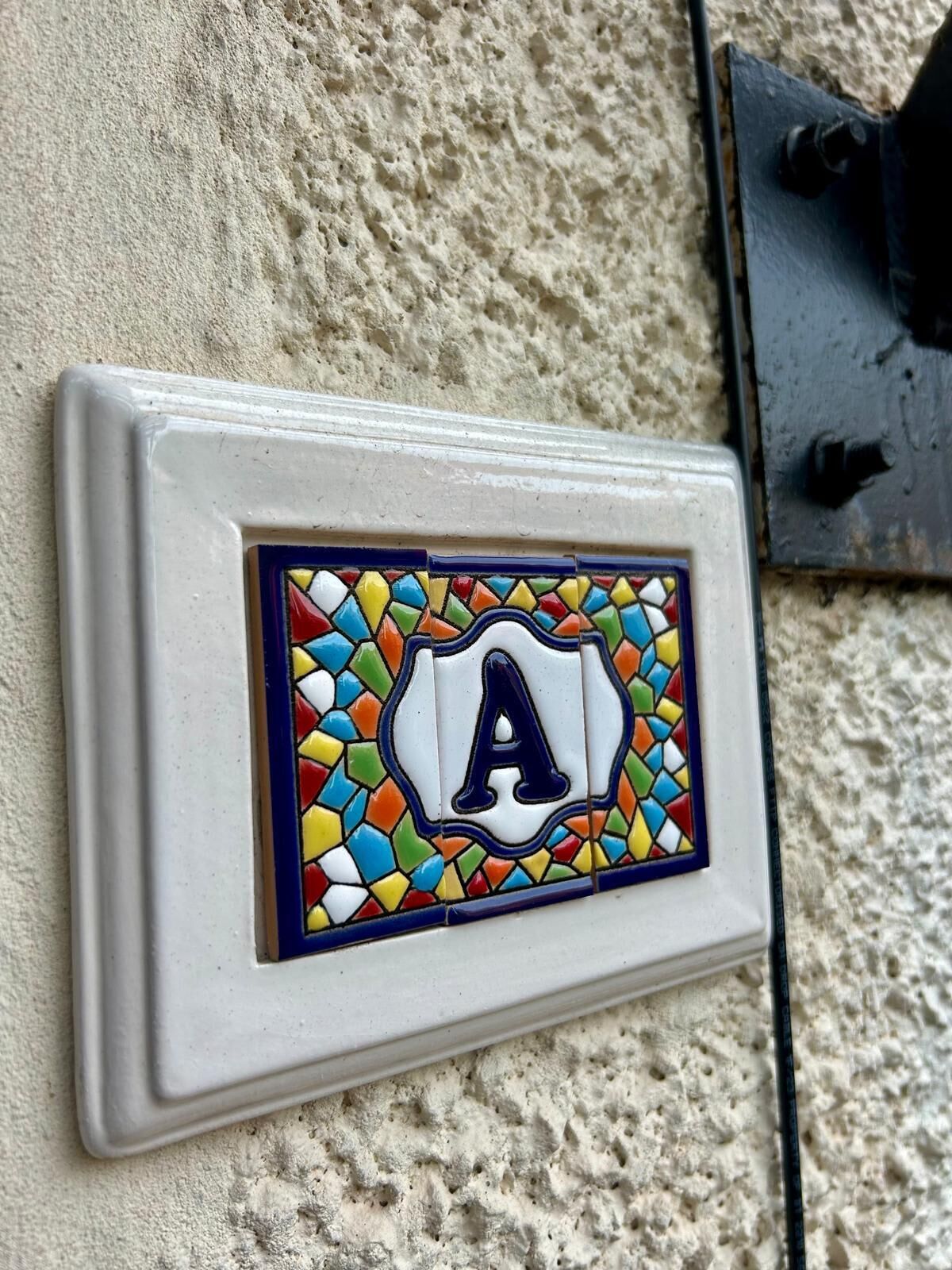 A wall-mounted light switch with a colorful mosaic tile featuring the letter 'A'.