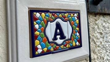 A wall-mounted light switch with a colorful mosaic tile featuring the letter 'A'.