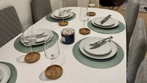 Ein Esszimmertisch ist gedeckt mit Tellern, Gläsern und Besteck, umgeben von gepolsterten Stühlen.