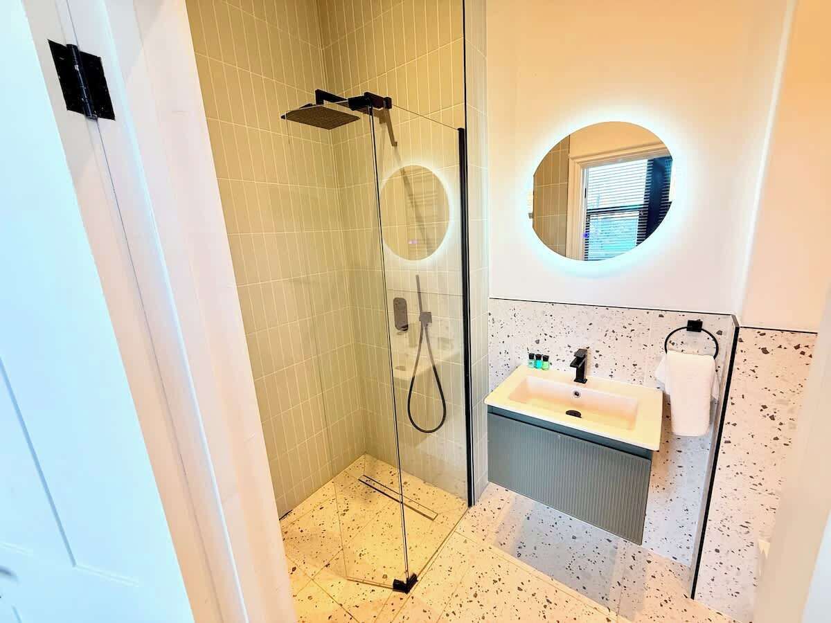 A modern bathroom with a glass-enclosed shower, a sink with a mirror, and a circular window above the sink.