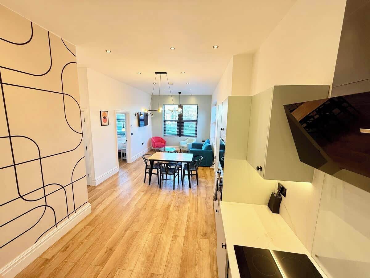 Eine moderne Küche mit Holzboden, einem Essbereich mit Tisch und Stühlen sowie einem Wohnbereich mit Sofa und Fernseher.
