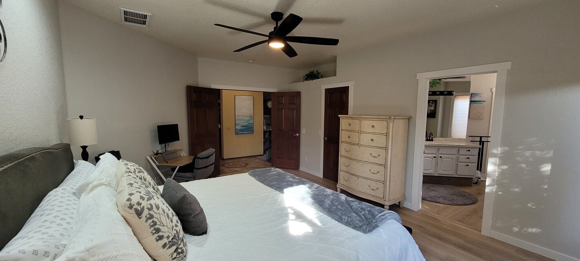 Un dormitorio con cama, escritorio, silla, armario y ventilador de techo.