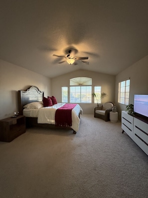 Ein Schlafzimmer mit Bett, Deckenventilator, Fernseher und Fenster.
