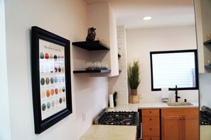 A kitchen with a framed color palette, a gas stove, wooden cabinets, and a window with blinds. - Chic Music City Retreat & Studio (Nashville)