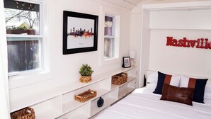 A bedroom with a bed, a cityscape picture, a wall-mounted lamp, and a shelf with baskets. - Chic Music City Retreat & Studio (Nashville)