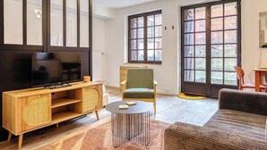 A living room with a TV, wooden entertainment unit, green armchair, and a sofa. - Gathéa, studio rénové pour 2 proche du Vieux marché (Rouen)