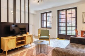 A living room with a TV, wooden entertainment unit, green armchair, and a sofa. - Gathéa, studio rénové pour 2 proche du Vieux marché (Rouen)