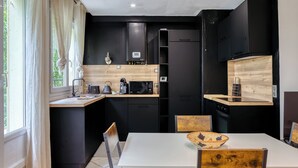 Una cocina moderna con armarios negros, una mesa de comedor blanca y detalles de madera.