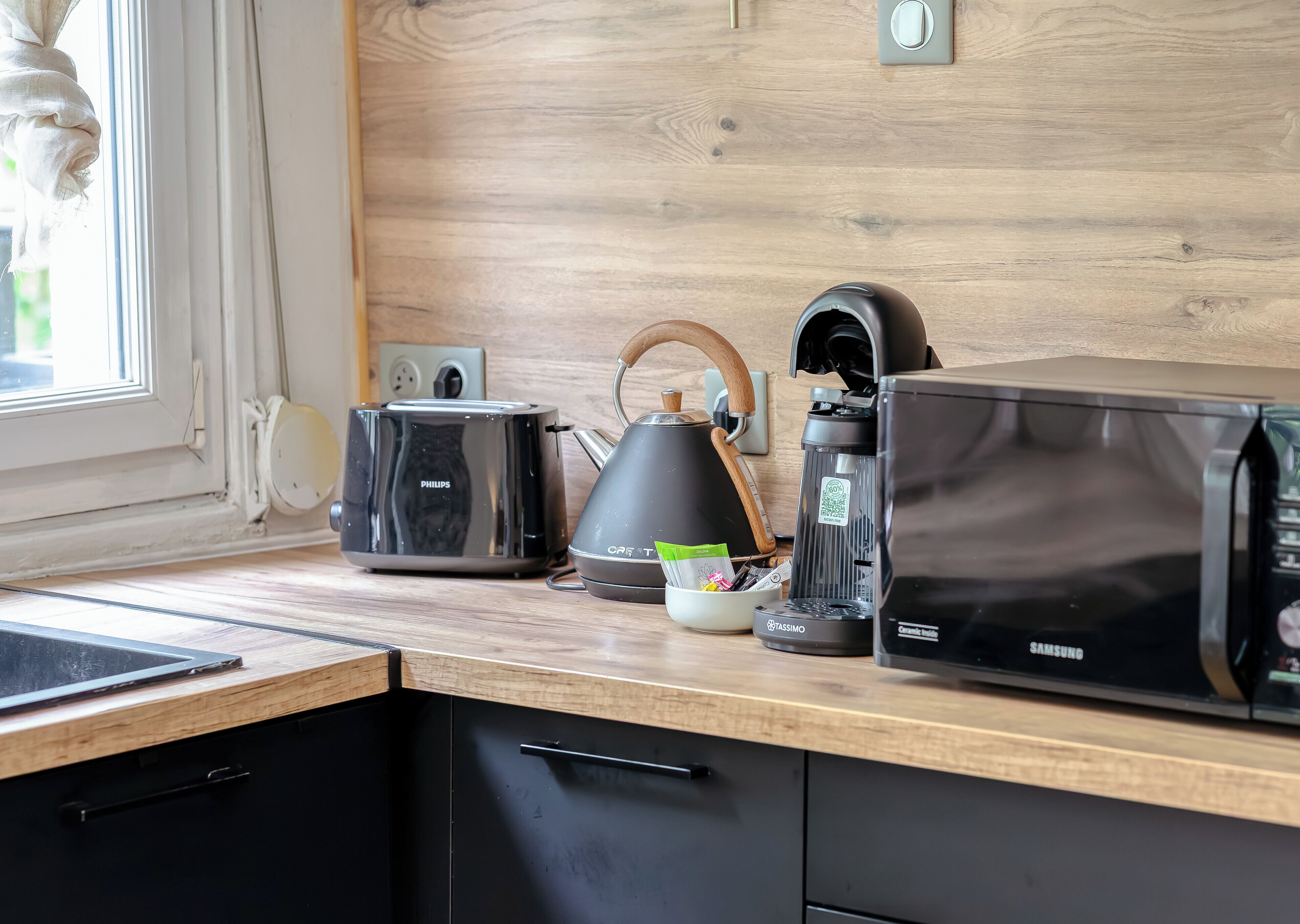 Una cocina con tostadora, hervidor, cafetera y microondas sobre una encimera de madera.