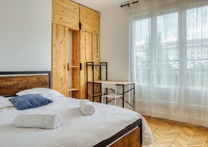 Ein Schlafzimmer mit einem Bett, einem Holzschrank, einem Schreibtisch und einem Fenster mit durchsichtigen Vorhängen.