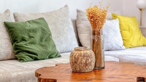 Una mesa de centro de madera con un florero y un frasco decorativo, colocada sobre un sofá con varios cojines.