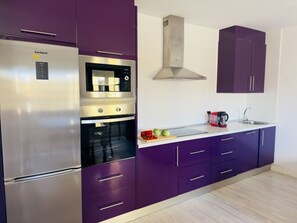 Eine moderne Küche mit Edelstahl-Kühlschrank, Backofen und Mikrowelle, lila Schränken und einer Edelstahl-Dunstabzugshaube.