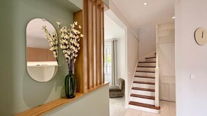 Una escalera con escalones de madera y barandillas blancas, un espejo redondo en la pared, y un jarrón con flores en un estante.