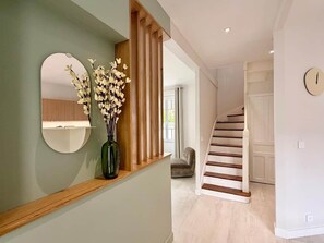 Eine Treppe mit Holzsitzen und weißen Geländern, ein runder Spiegel an der Wand und eine Vase mit Blumen auf einem Regal.