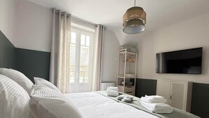 Una habitación de hotel con cama, televisión, armario y ventana con cortinas.