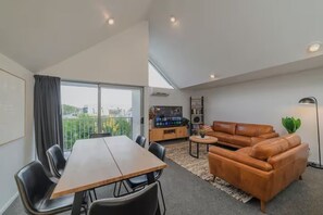 A modern living room with a dining table, leather sofa, and a flat-screen TV. - Modern Comfort in Central Christchurch (Christchurch)
