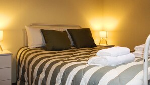 A hotel room with a bed, pillows, a nightstand, and a lamp.