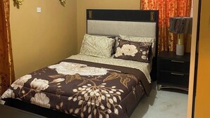 A bedroom with a bed, a nightstand, a lamp, an air conditioning unit, and a painting on the wall.