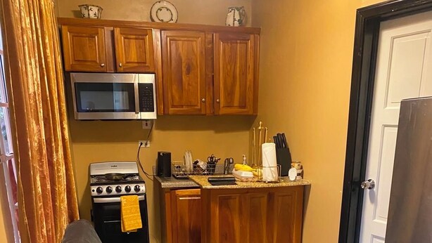A compact kitchen with wooden cabinets, a microwave, a stove, and a small island with kitchen utensils.