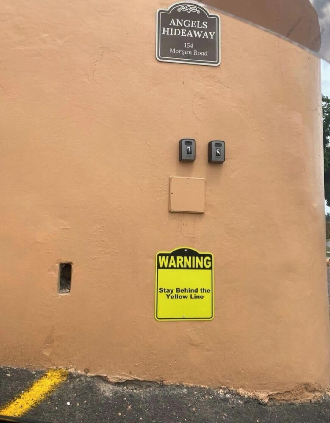 Fachada de edificio con un letrero que dice 'Angels Hideaway 154 Morgan Road' y un cartel de advertencia que indica 'Manténgase detrás de la línea amarilla'.