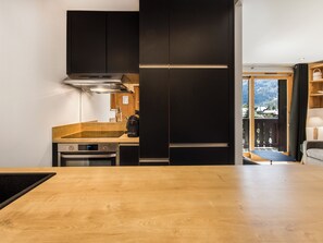 A modern kitchen with dark cabinetry, a wooden countertop, and a view of a balcony. - Fermes de Méribel Delys #2D2 - 6 guests - Ski in - Ski out (Les Allues)