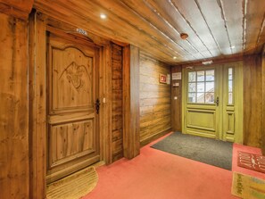 A wooden interior hallway with a green door, a wooden door with a carved head, and a red carpet. - Fermes de Méribel Delys #2D2 - 6 guests - Ski in - Ski out (Les Allues)