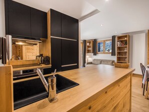 A modern kitchen with black cabinets, a wooden countertop, and a built-in stove. - Fermes de Méribel Delys #2D2 - 6 guests - Ski in - Ski out (Les Allues)