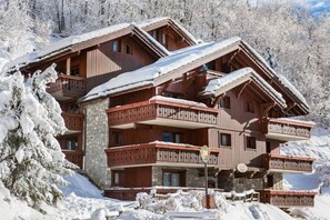 Una cabaña de madera de varios pisos con balcones, rodeada de árboles cubiertos de nieve.