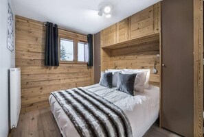 Una habitación con paneles de madera, una cama, una ventana con cortinas y un radiador blanco.