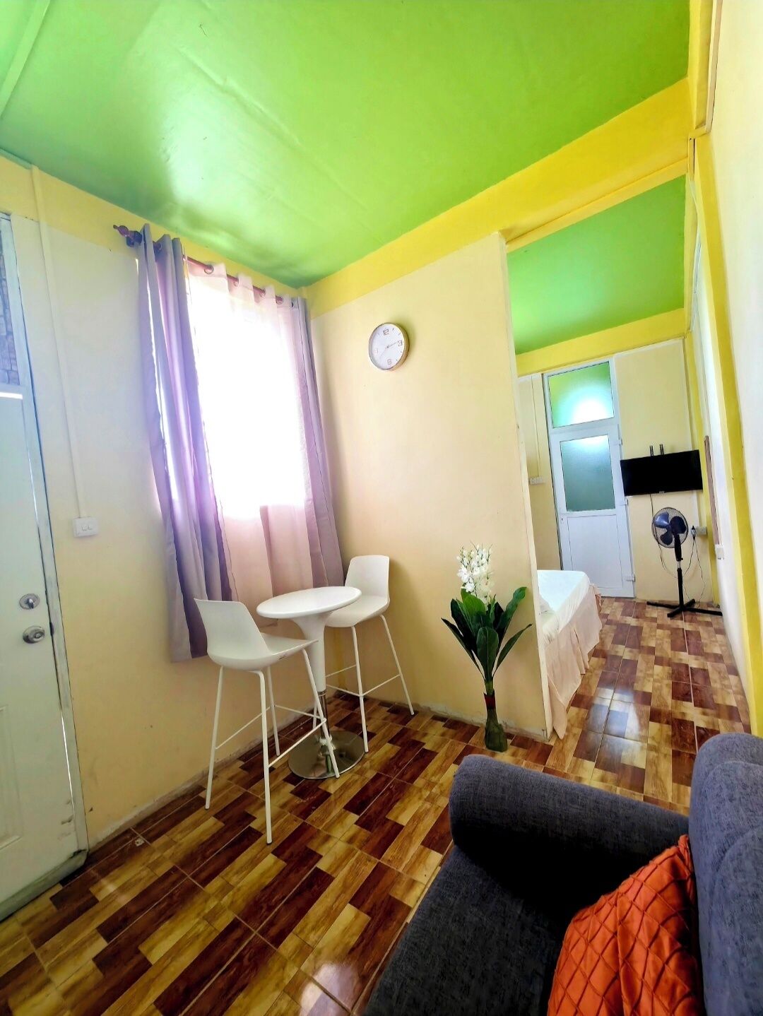 A room with a dining table and chairs, a sofa, a clock on the wall, and a fan.