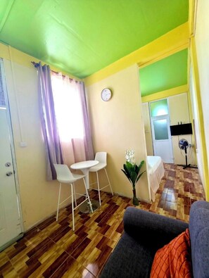 Une pièce comprenant une table à manger et des chaises, un canapé, une horloge au mur et un ventilateur.