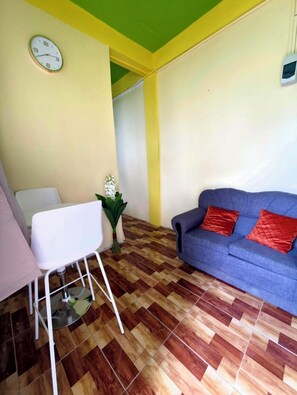 Una habitación con un sofá azul, una silla blanca, un reloj en la pared y una planta pequeña.