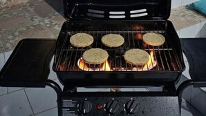 En utomhusgrill där hamburgare tillagas, en pool med blått ljus och ett inhägnat område med solstolar.