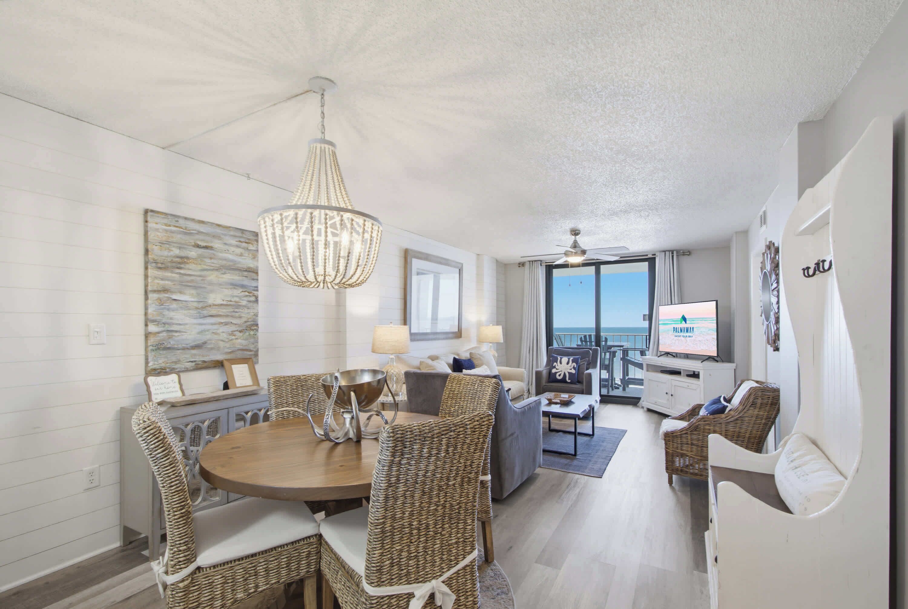 A modern living room with a dining area, a television, and a view of the ocean.