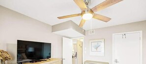 Ein Zimmer mit Deckenventilator, Fernseher, Tür und einem gerahmten Bild an der Wand.