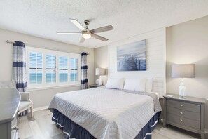 A hotel room with a bed, a desk, a chair, a ceiling fan, a window with curtains, a painting on the wall, and a nightstand with a lamp. - Super Clean, Pool, Beach, Dining, Fun (Orange Beach)