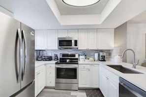 A modern kitchen with stainless steel appliances, white cabinetry, and a tiled backsplash. - Super Clean, Pool, Beach, Dining, Fun (Orange Beach)