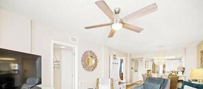 Ein großzügiges Wohnzimmer mit Deckenventilator, Fernseher und Essbereich mit einer Kronleuchter.