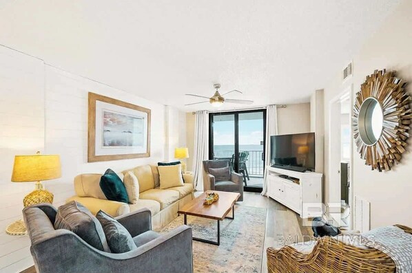 Ein modernes Wohnzimmer mit einer Couch, Sesseln, einem Couchtisch, einem Fernseher und einem Balkon mit Blick.
