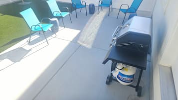 Patio esterno con barbecue, sedie e bombola di propano.