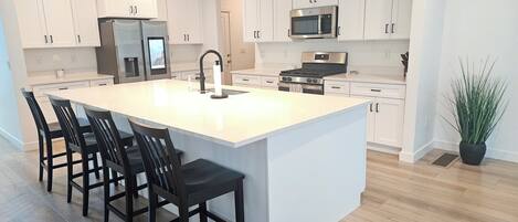 A modern kitchen with white cabinets, a large island with bar stools, a stainless steel range, and a microwave.