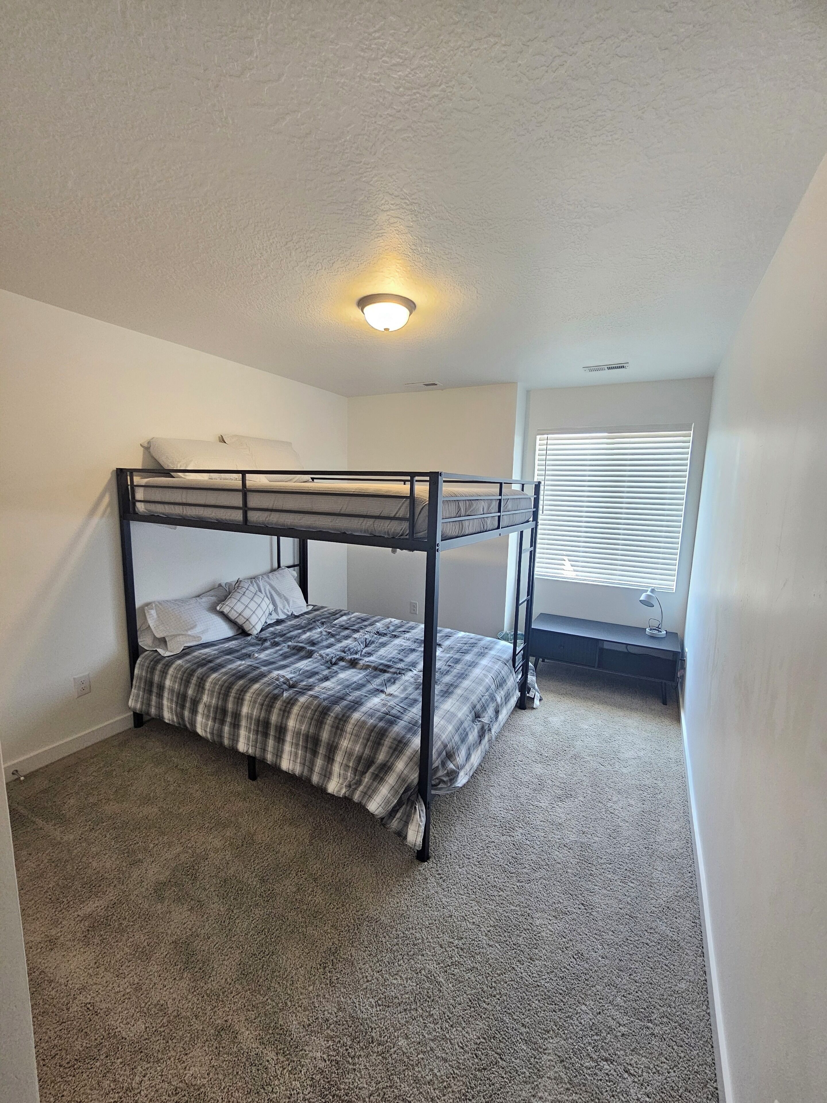 Quarto com beliche, piso coberto por carpete, luminária no teto e janela com persianas.