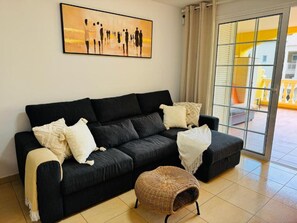 Ein schwarzes Sofa mit weißen Kissen, ein gewobener Pouf und ein Gemälde mit Silhouetten an der Wand.