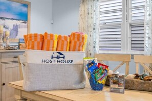 Eine Küchenzeile mit einer Tasche mit dem Aufdruck 'HOST HOUSE', die Snacks enthält, einem Buch mit dem Titel 'DIREKT BUCHEN UND 10% SPAREN' und einem Fenster mit Jalousien.