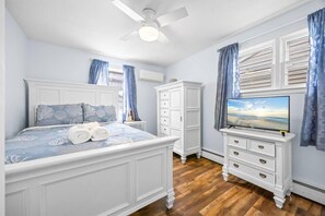 Ein Schlafzimmer mit einem Bett, einem Schminktisch, einem Fernseher und einem Deckenventilator.