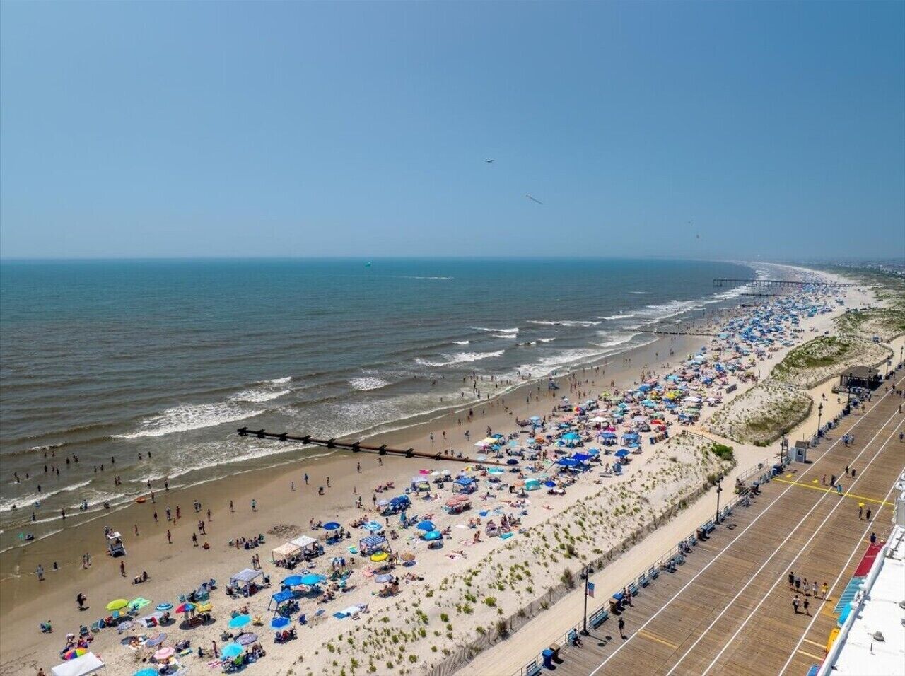 Una playa con un paseo marítimo de madera, sombrillas y gente.